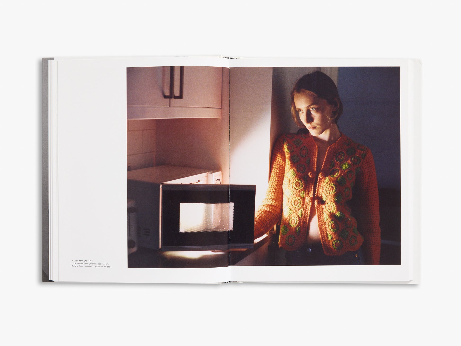 Open book showing a person wearing a patterned sweater in a room with a microwave.
