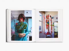 Open book showing two photos: one of a person holding flowers in a kitchen, the other of a room with a colourful sculpture.